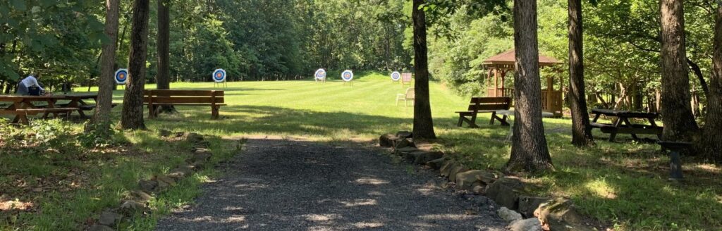 A row of archery targets across a grass field, with the field archery gazebo on the right, framed by trees